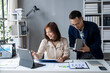 © Wasana - A man and a woman are sitting at a desk with a laptop and a book
