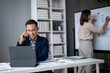 © Wasana - A man is talking on his cell phone while sitting at a desk with a laptop