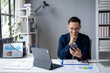 © Wasana - A man is sitting at a desk with a laptop and a cell phone