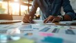 © Naret - Close-up of a person analyzing data and creating reports at a desk, surrounded by charts and documents, in an office environment.