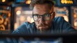 © Naret - Focused engineer working in control room, surrounded by advanced technology, bright screens, and modern equipment, wearing glasses.