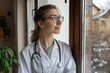 © volga - Smiling female doctor looking out a window in a clinic setting