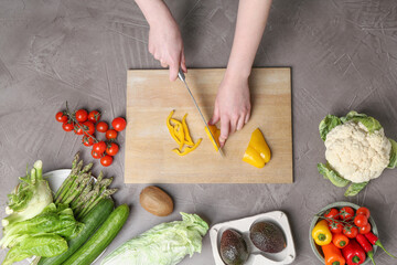 Healthy food. Woman cutting pepper at gray textured table, top view