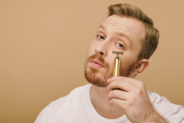 Wall Mural - A man in casual attire holding face roller in front of his face.