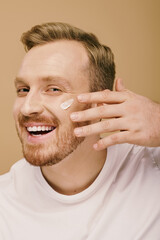 Wall Mural - A man in casual attire is happily applying cream to his face.