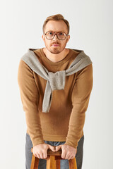 Wall Mural - Handsome man in sweater and glasses poses on stool.