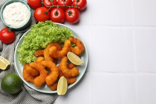 Delicious breaded fried shrimps served on white tiled table, top view. Space for text