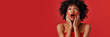 © wolfhound911 - an African American woman in an elegant red evening gown, showing disbelief with her hands on her cheeks on a red studio background