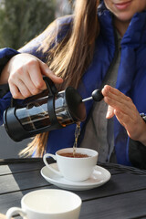 Wall Mural - Woman pouring tea into cup at black wooden table in outdoor cafe, closeup