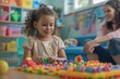 © evgenia_lo - A mixed-race girl with curly hair playing with blocks and shapes at a preschool, with a Caucasian woman smiling in the background.