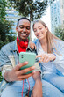 © Jose Calsina - Vertical. Young multiracial couple having fun with a cellphone to browsing on internet. Two teenage friends using a smart phone to share on the social media app. Young people watching a mobilephone
