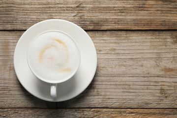 Wall Mural - Tasty cappuccino in coffee cup on wooden table, top view. Space for text