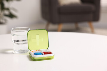 Wall Mural - Different pills in organizer and glass of water at white table, closeup. Space for text