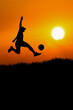 © STOCK PHOTO 4 U - Silhouette of Person Kicking Soccer Ball at Sunset with Vibrant Orange Sky and Sun in Background