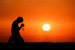 © STOCK PHOTO 4 U - Silhouette of Person Kneeling in Prayer Holding Cross Against Vibrant Orange Sunset Sky