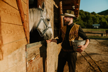 Wall Mural - Young horse breeder is feeding a horse near stall while holding bucket