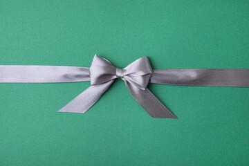 Wall Mural - Grey satin ribbon with bow on green background, top view