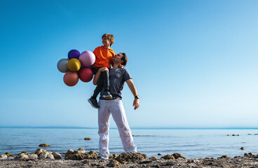 Wall Mural - Father holding his son with balloons on lake shore on summer day