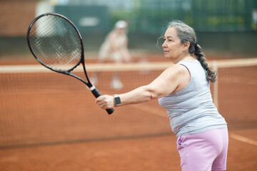 Wall Mural - Elderly female tennis player serving ball during game on tennis court