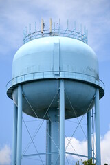 A light blue, very tall water tower with a light blue sky background.