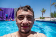 © Viga - A man in a pool, resting his chin on the edge while smiling at the camera. The scene is bright and sunny