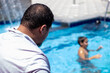 © Viga - A man in a pool, watching others swim. The background shows a lively poolside scene on a sunny day