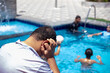 © Viga - A man in a pool covering his ears, possibly trying to get water out. The scene is lively and bright, indicating a fun day by the poolside