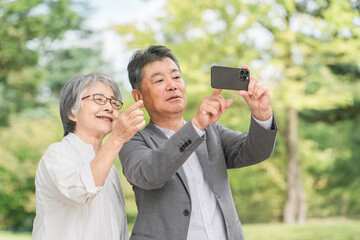 Canvas Print - 屋外でスマホを使って写真や動画を撮る高齢者夫婦（旅行・老後・お出かけ・公園・記念写真）
