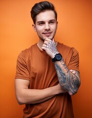 Wall Mural - young man with arm tattoos on isolated orange background arms crossed close up cool guy