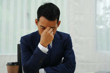 stressed businessman is sitting at his office desk, looking worried while working on his laptop. Overworked and frustrated, he faces financial problems and job pressures in his corporate banking role