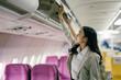 © Parichat - Businesswoman Storing Luggage in Overhead Compartment on Airplane During Flight