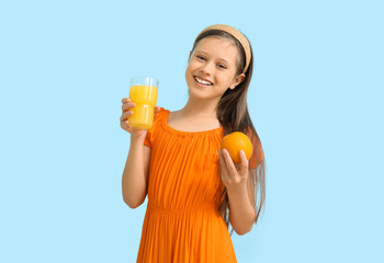 Little girl with glass of juice and orange on blue background