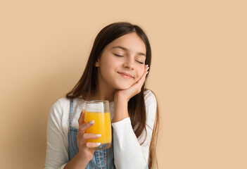 Wall Mural - Little girl with glass of orange juice on beige background