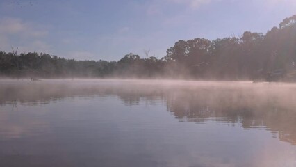 Wall Mural - Mist in the early morning sweeps over the surface of a lake on the Severn River showing reflections and calm water with a cloudy sky background near Stanthorpe in Queensland, Australia.