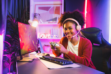 Wall Mural - African American girl gaming streamer team winner playing online fighting with Esport wearing headphones in neon lighting room. Talking other players planing strategies to win competitors. Tastemaker.