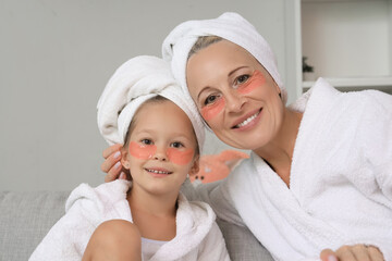 Poster - Little girl and her grandmother with under-eye patches at home, closeup