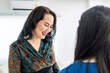 © TeTe Song - Asian woman comes to reception desk in clinic lobby area and makes appointment with doctor. Female administrator talks with patient at information counter. Medical staff work in medical center