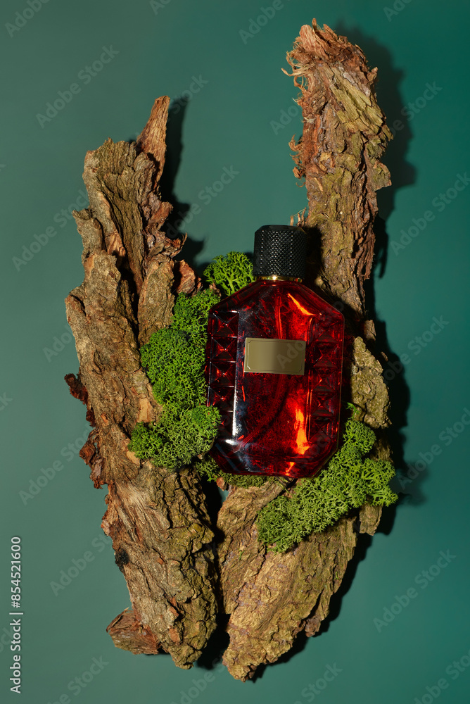 Red bottle of perfume and tree bark on green background
