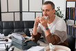 © Pixel-Shot - Mature man with vintage typewriter and cup of coffee sitting at table in office