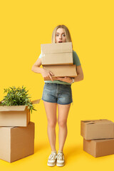 Shocked young woman with cardboard boxes on yellow background. Moving into new house concept