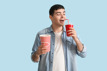 Wall Mural - Happy young man with popcorn and soda on blue background