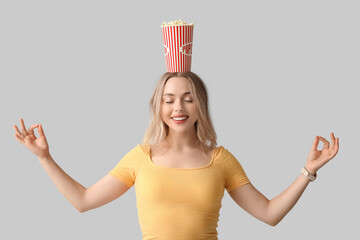 Poster - Young woman with bucket of popcorn meditating on white background