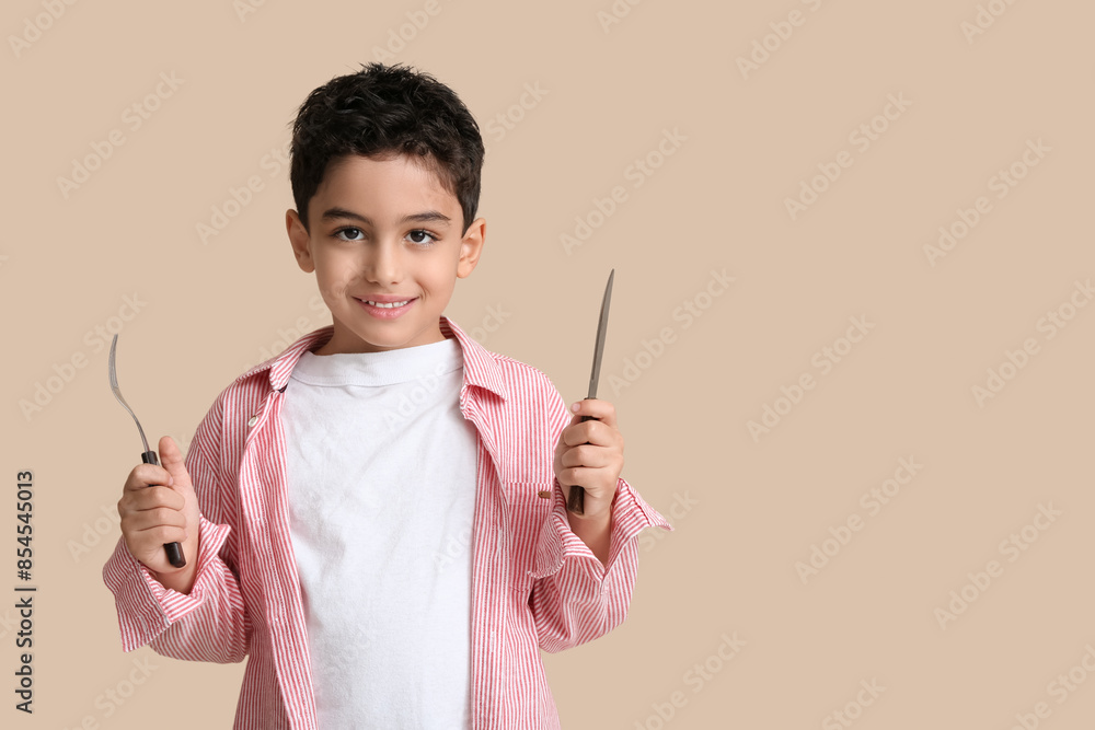 Cute little boy with fork and knife on beige background