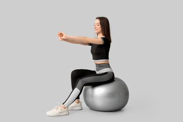 Wall Mural - Sporty young woman training on fitball against light background