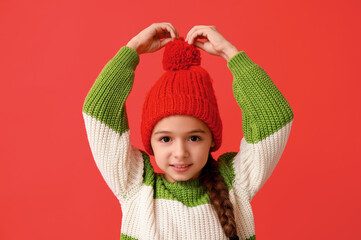 Wall Mural - Cute little girl in warm hat on red background