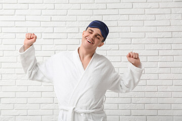 Canvas Print - Portrait of handsome young man in bathrobe and sleeping mask stretching on white brick background