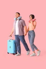 Sticker - Beautiful young happy couple of tourists with suitcase and travel pillows on pink background