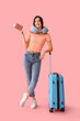 © Pixel-Shot - Beautiful young happy female tourist with suitcase, passport and travel pillow on pink background