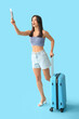 © Pixel-Shot - Beautiful young happy female tourist with suitcase, passport and ticket on blue background