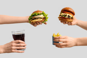 Poster - Female hands with tasty burgers, french fries and glass of cola on white background